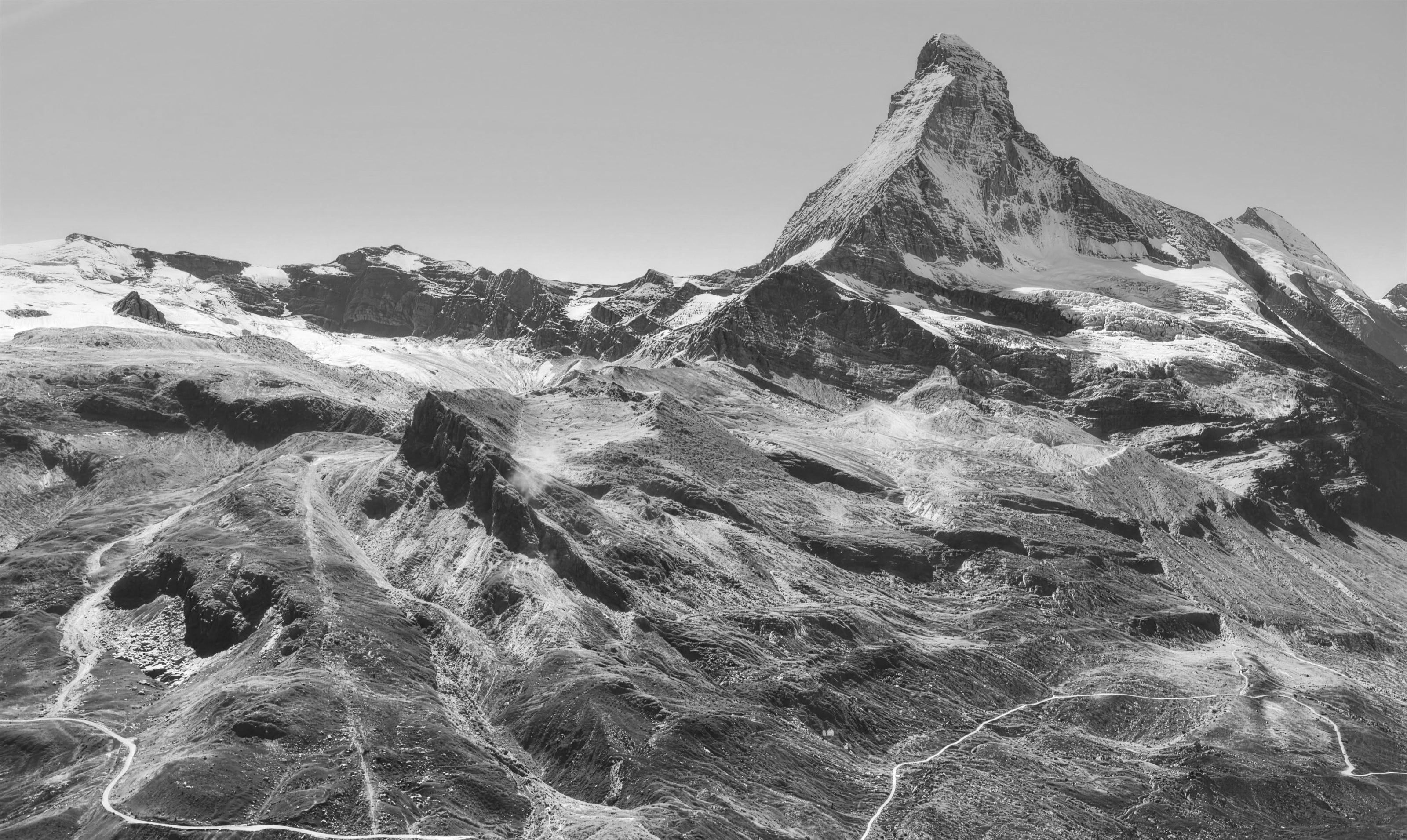 Das Matterhorn in Schwarzweiss, davor Gletscher, Geröllhänge und Bergwege